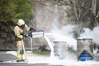 Yangını söndürmek için köpük kullanan itfaiyeci dumanlı bir doğal ortamda erimiş yağ tenekesinde.