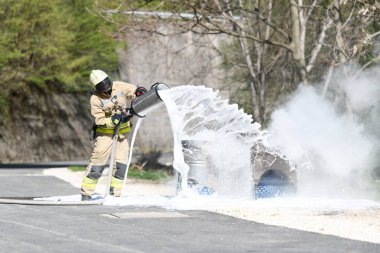 Profesyonel itfaiyeci yol ve evlerin yakınındaki metal bir yağ bidonunda alevlerle savaşıyor.