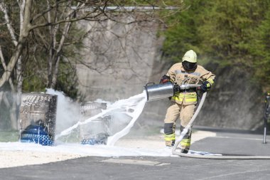 Yangını söndürmek için köpük kullanan itfaiyeci dumanlı bir doğal ortamda erimiş yağ tenekesinde.