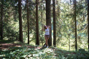 Relaxed Woman Posing By A Tree In A Sunlit Forest With Accessories clipart