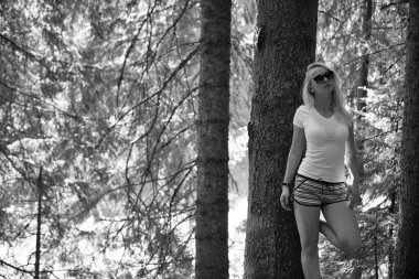 Güneşli bir ormanda aksesuarlı bir ağacın yanında rahatlamış kadın pozu