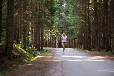 Geniş yollar ve doğa ile ormanda yürüyüş yapan bir kadın.
