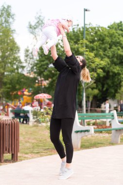 Anne, güneşli bir günde bebeği havaya kaldırıyor.