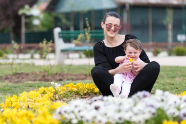 Parkta oturan anne ve bebek Etrafı çiçeklerle çevrili