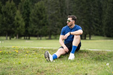 Sporcu güzel bir günde çimenlik ve ormanla birlikte çimenlikte mola veriyor.