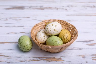 Yeşil, beyaz ve sarı kahverengi benekli yumurtalar eski ahşap beyaz arka planda hasır plakanın içinde ve yakınında. Paskalya kartı, seçici odaklanma.