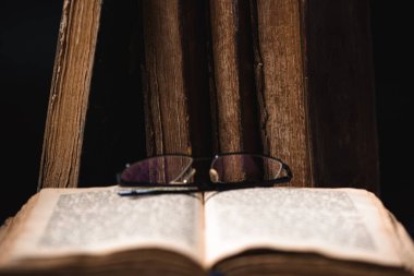 An open blurred page with hebrew religious text, glasses and old worn shabby leather-bound Jewish books Chumash in the background. The concept of studying and reading Torah. Selective focus. Closeup