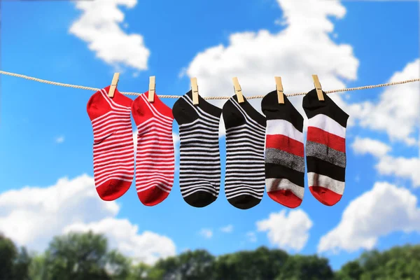 Clean washed striped socks hanging on clothesline to dry outdoors on sunny summer day. Clothesline with red, gray and white socks against blue sky