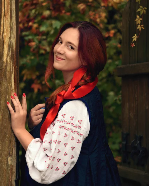 明るい若い赤毛の女性は 伝統的なウクライナの刺繍の服を着て カメラを見て彼女の髪に赤いリボンで笑顔 ヴィンテージの衣装 半角像 — ストック写真