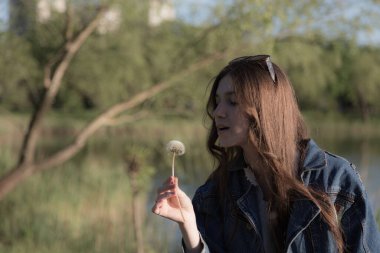 Elinde karahindiba olan güzel bir kızın portresi. Parkta bir yerde oluyor. Yakın plan..