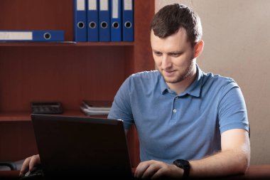 Yoğunlaşmış genç bir adamın portresi. Fotoğraf ofiste çekildi ve arka planda klasörler var. Yakın plan..