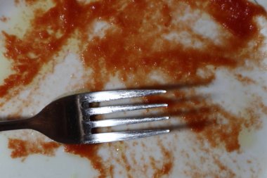 İçinde domates sosu ya da ketçap olan boş beyaz tabak. Beyaz arka planda bir çatal. Yakın plan..