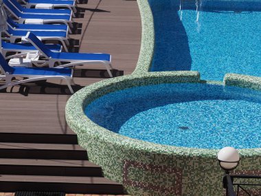 Mavi ve beyaz mozaikleri ve güneşli yatakları olan açık havada yuvarlak bir havuz.