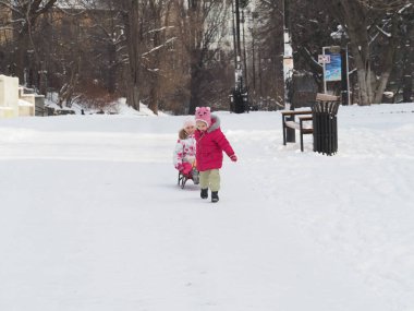 a younger sister pulls a sled with an older sister in a snowy park