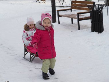 a younger sister pulls a sled with an older sister in a snowy park