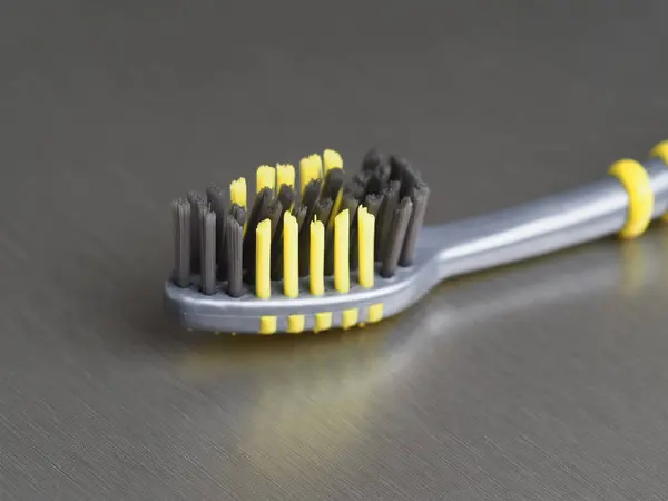 金属の背景のクローズアップに黒と黄色のブリストルが付いている灰色の歯ブラシ — ストック写真