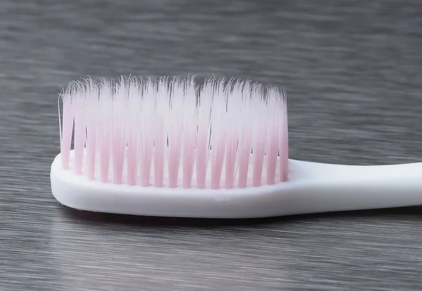 金属の背景にピンクのブリストルが付いている白い歯ブラシ — ストック写真