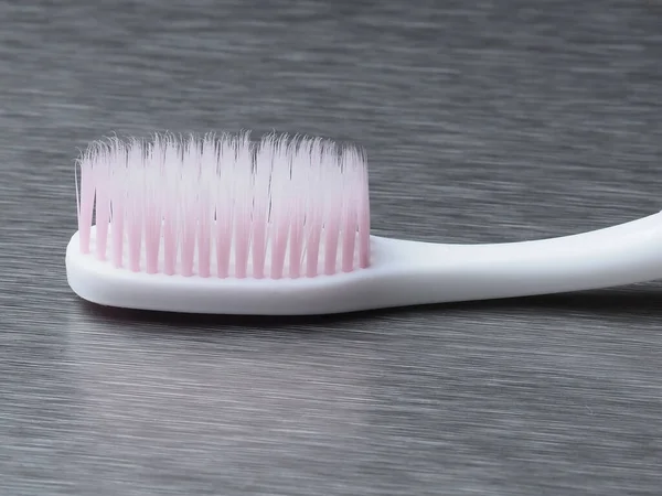 金属の背景にピンクのブリストルが付いている白い歯ブラシ — ストック写真