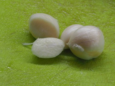 Yeşil plastik kesim tahtasında soyulmuş sarımsak karanfilleri.