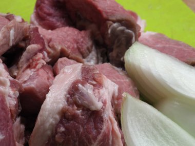 Kabaca doğranmış soğan ve sarımsak karanfilli yeşil bir plastik doğrama tahtasındaki büyük domuz parçaları.
