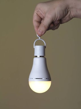 Avuçta bej bir arka plan ışığı olan birinin elinde açık bir LED şarj edilebilir lamba. Bej arka planda LED lamba.