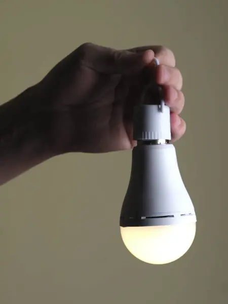 A switched-on LED rechargeable lamp in the hands of a person on a beige backgroundLight in the palm: LED lamp on a beige background