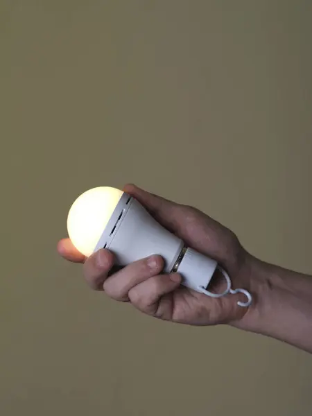 A switched-on LED rechargeable lamp in the hands of a person on a beige backgroundLight in the palm: LED lamp on a beige background