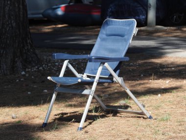 A blue folding chair among nature and cars clipart