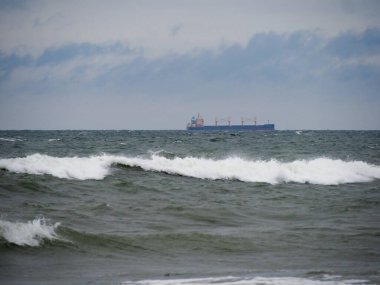 Kargo Gemisi Ufukta Bulutlu Gök Altında Çalkantılı Deniz Dalgaları Ortasında, Doğanın Gücü ve Küreselleşmesini Sembolize Ediyor
