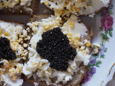 Three Open-Faced Sandwiches with Black Caviar and Egg on Floral Patterned Plate clipart