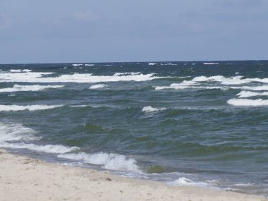 Mavi gökyüzünün altında dalgaları olan kumsal, doğal güzellik ve sükunetle dolu bir yaz günü.