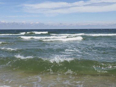 Mavi gökyüzünün altında dalgalar ufukta süzülen beyaz bulutlar