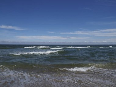 Denizde dalgalar, mavi gökyüzünün altında, beyaz bulutlar ve ufukta, yaz günü huzurlu bir tatil için.