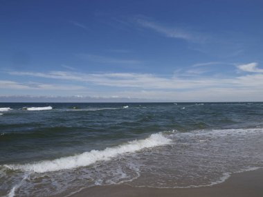 Dalgalar ve kumlu plajlı doğal deniz manzarası mavi gökyüzü ve güneş altında