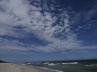 Mavi gökyüzünde dalgalar ve bulutlarla kumsal manzarası