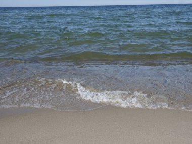 Sakin deniz, temiz bir kumsal, berrak bir gökyüzünün altında.