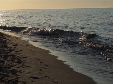 Sahilde sakin dalgalar akşam güneşinin altında Suyu yansıtıyor