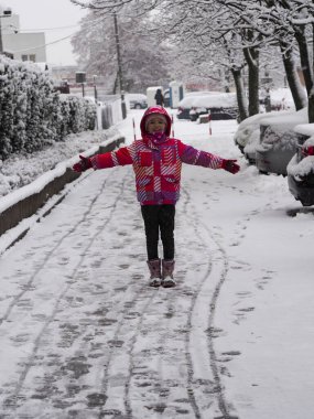 Child Enjoying Snowy Winter Day in Colorful Jacket on Snow-Covered Street clipart