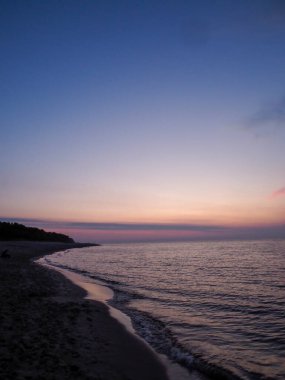 Sakin bir plajda, sakin bir gün batımı. Yumuşak dalgalar ve dramatik bulutlar.