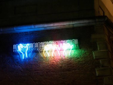 Renkli el şekilli mavi, yeşil ve sarı renkli bir duvara neon ışığı yerleştirilmiş.