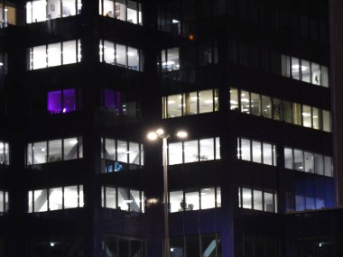 Geceleri aydınlık pencereleri ve sokak ışıklarıyla modern ofis binası