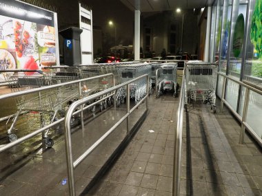 Nighttime view of shopping carts in a supermarket parking lot with wet pavement clipart