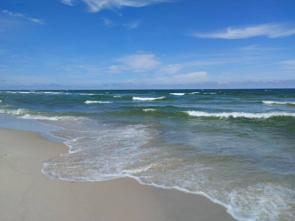 Спокойный прибрежный пейзаж с мягкими волнами, выходящими на пустой песчаный пляж под голубым небом