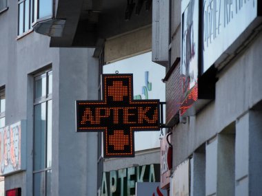 Şehir merkezindeki Şehir Binası Cephesi 'nde Aydınlatılmış Turuncu Eczane Çapraz İşareti