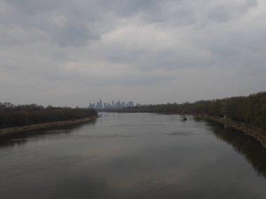Bulutlu Gökyüzü Altında Uzak Şehir Skyline ile Serene Nehri Manzarası Panoramik Doğa Görünümü Sunuyor