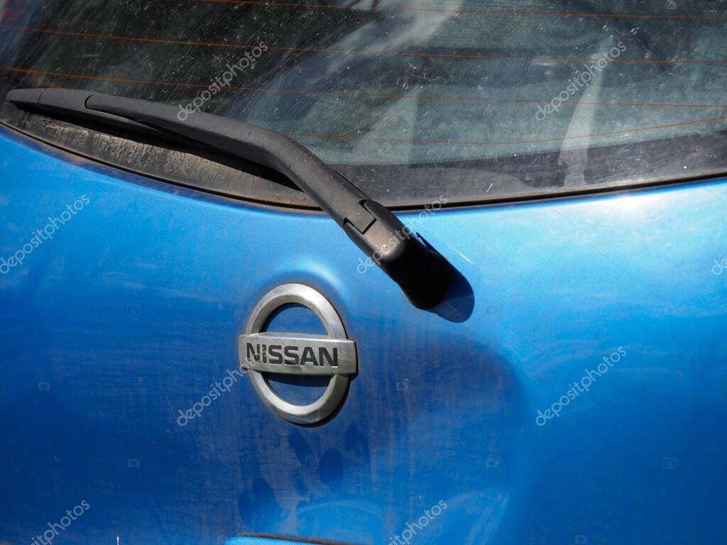 Close-Up of Nissan Logo on Blue Car Hood Showing Japanese Automotive Brand Emblem in Rain Droplets