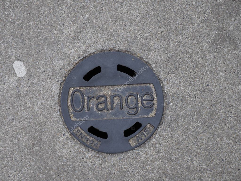 Close-up of Circular Orange Telecom Manhole Cover on Gray Stone Pavement