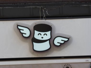 Şehirdeki Beyaz Bina Cephesi 'nde Kanatlar Logosu olan Quirky Kahve Kupası Karakteri