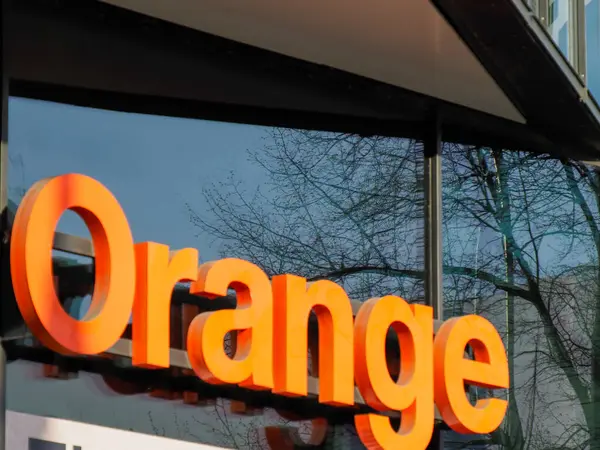 Aydınlatılmış Turuncu Telekomünikasyon Şirketi Logosu Arkadaki Ağaçlarla Modern İnşaat Dış Alanı