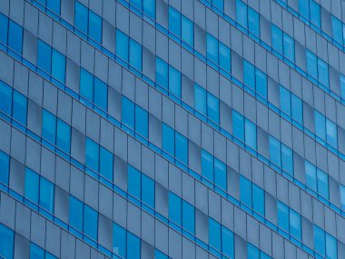 Mavi cam gökdelenin soyut deseni bulutları ve gökyüzünü yansıtıyor ve kusursuz geometrik bileşim oluşturuyor